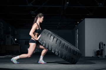 Fototapeta na wymiar Female fitness model flipping a tyre in a gym