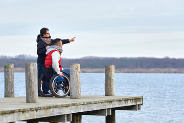 Frau am Steg am See mit Rollstuhlfahrer
