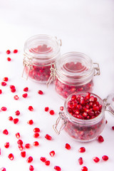 Grains of red juicy pomegranate closeup and in jars on white bac
