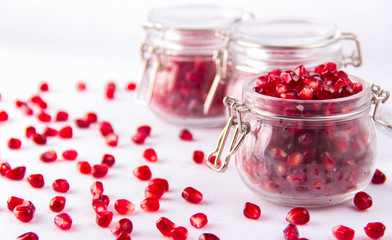 Grains of red juicy pomegranate closeup and in jars on white bac