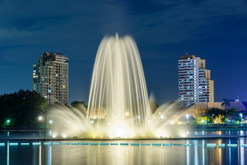 Obraz premium An ornamental fountain arches gracefully into the air at night above the lake at Queen Sirikit National Convention Center in Downtown Bangkok, Thailand. 