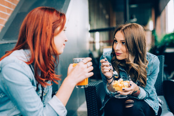 Two girls sitting in a bar having fruit salad and juice talking - best friends, chatting, gossip...