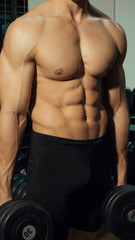 Fototapeta na wymiar Muscular guy in the gym with dumbbells