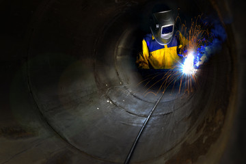Industrial worker welding metal and many sharp sparks inside piping construction with confined...