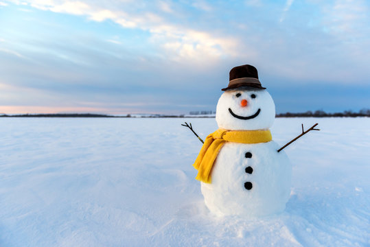 Little cute snowman in a knitted hat and scarf on snow on a sunny