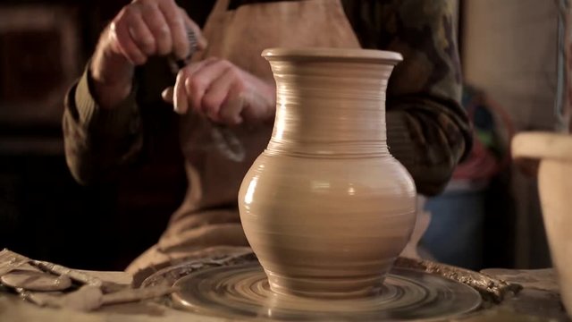 close up of potter's hands designing pattern on traditional pottery by chisel with blurry other equipments on desk, clay,