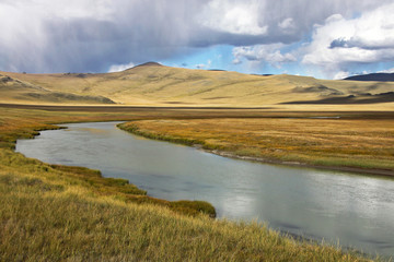 White wide river on a background of rocky hills under white clouds and blue sky, Plateau Ukok, Altai mountains, Siberia, Russia