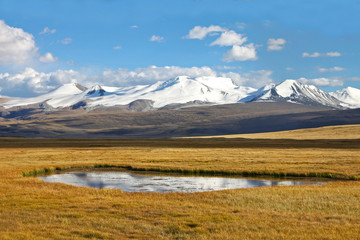 Fototapeta premium Landscape steppe shore lake with dry yellow grass and high mountain range with snow glaciers ice, Ukok Plateau, Altai, Siberia, Russia