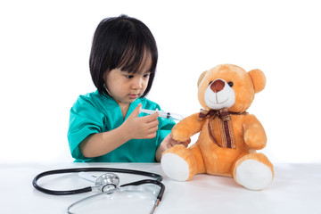 Asian Chinese little doctor girl giving injection to teddy bear