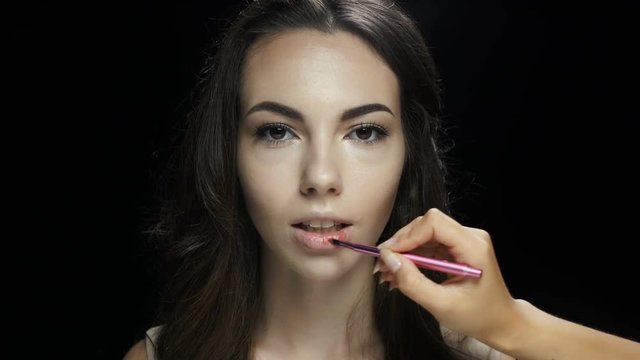 Make up artists hand with brush applying lipstick on smiling female face