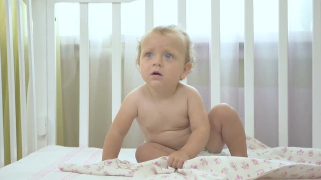 Little girl sitting in a baby cot.