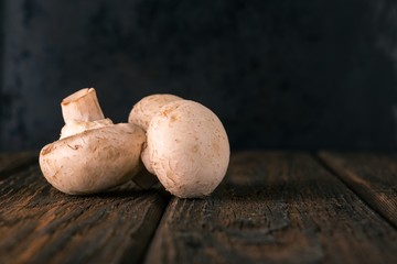 Three champignon mushrooms on dark wooden board