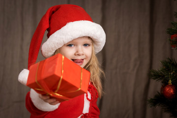 little girl in a Santa suit near Christmas tree
