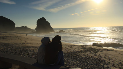Couple in a beach in Portugal at the sunset with a big rock in background. Santa Cruz, Portugal