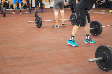 Gym: barbells on a broun floor and feet in sneakers.