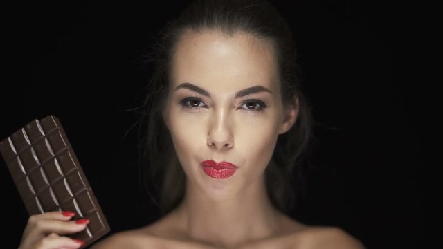 Attractive young woman with red lipstick biting dark chocolate bar
