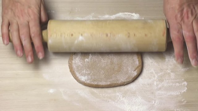 Rolling the dough by wooden roller on the wooden board