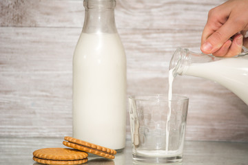 Milk poured into glass from woman hand on wooden background. fresh milk