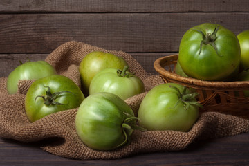 unripe green tomatoes in a wicker basket on wooden table with sacking