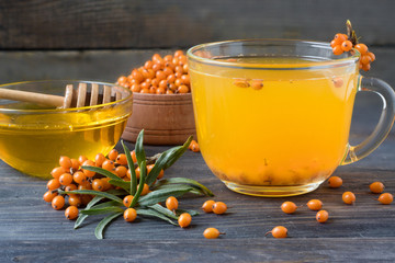Tea of sea-buckthorn berries with honey and a branch on wooden background