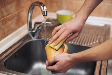 Man washing the orange cup in the kitchen sink