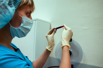 assistant nurse in a mask in medical lab picked up a disposable flask with blood tests. A flask...