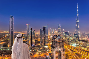 Homme arabe regardant le paysage urbain de nuit de Dubaï avec une architecture futuriste moderne aux Emirats Arabes Unis
