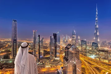 Foto auf Acrylglas Dubai Arabischer Mann, der das Nachtstadtbild von Dubai mit moderner futuristischer Architektur in den Vereinigten Arabischen Emiraten beobachtet