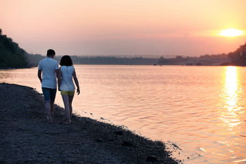 Romantic portrait of attractive couple in love hugs at the sunset . Against the backdrop of the sea and setting sun. Silhouette