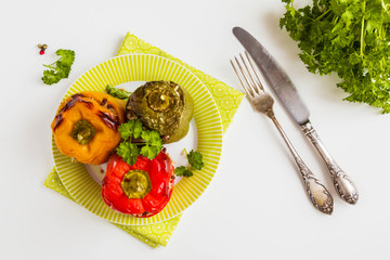 Baked bell peppers, yellow, red and green ones, stuffed with minced meat and rice. Fresh parsley, white table, top view.