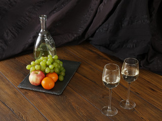 Still life, Jar of wine, two glasses with wine on a table, and grapes, oranges and an apple on a stone board.