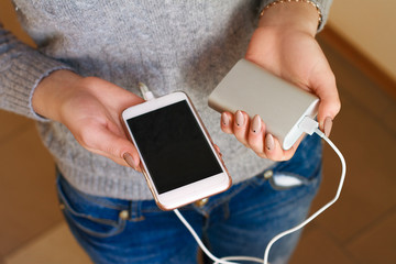 Two girls hands hold of the phone and charger. Powerbank and smartphone in girl's hands. Energy charger power bank smart phone. Still life modern digital concept. - Powered by Adobe