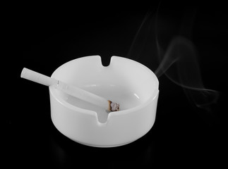 White ashtray with cigarette and smoke on the black background