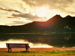 Empty bench at spring mountain lake. The coast with mountains at horizo