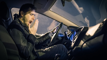 Tired man is yawning and driving a car at night.