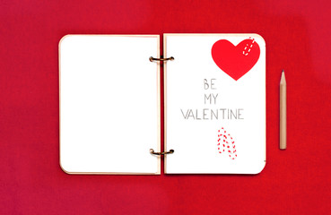 Opened blank notepad on red background. Valentine's hart