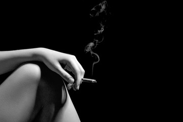 female hand with smoking cigarette on naked knee at black background with copyspace, monochrome
