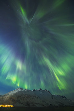 A coronal burst of aurora borealis (Northern Lights) during a solar storm in Northern Norway above a snowy mountain