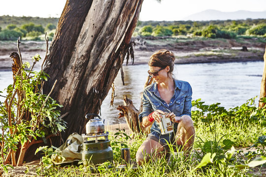 A young woman boils water for coffee in the early morning light while camping in Samburu National Park, Kenya,East Africa