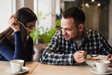 Funny couple eating noodles in cafe. He don't want to share his food with girlfriend