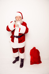 Shh! Santa Claus with christmas bag talking on phone