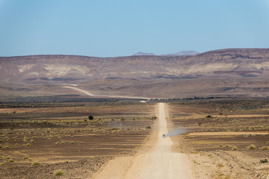 A 4x4 car leaves a cloud of dust as it apporachs along the long dusty road to the Fish River Canyon, Namibia