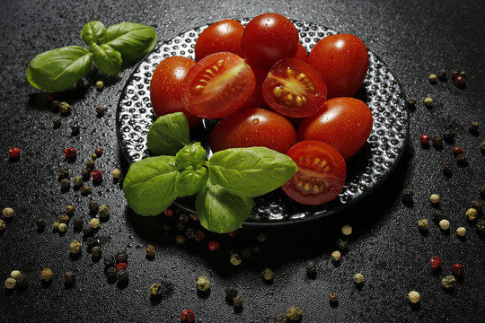 cherry tomatoes on a plate with basil and chili pepper on a blac