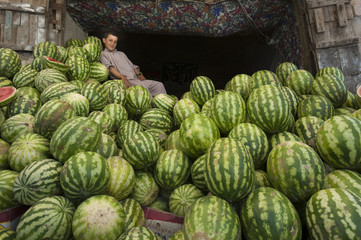 A boy in a market rests on a giant pile of water melons, Herat, Afghanistan