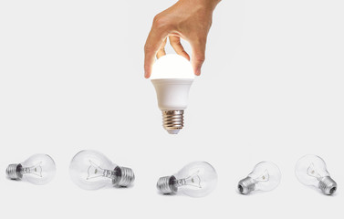 Hand holding a turned on LED light bulb over old incandescent light bulbs / Using economical and...