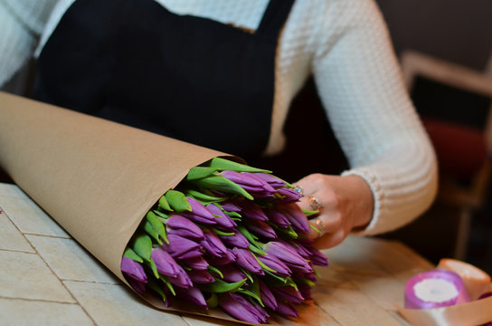 A woman makes bouquet of purple tulips. Blurred background.