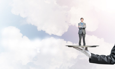 Confident businessman presented on metal tray against blue sky background