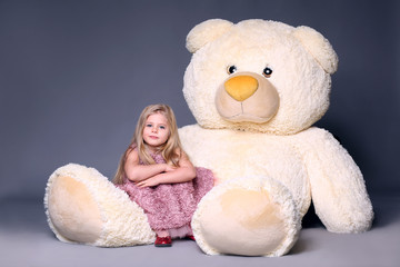 Little model in dress sitting on the big teddy's leg