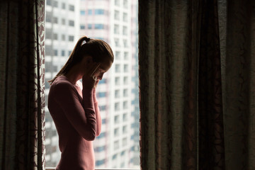 Fototapeta na wymiar Sad, confused and stressed woman standing next to her window.