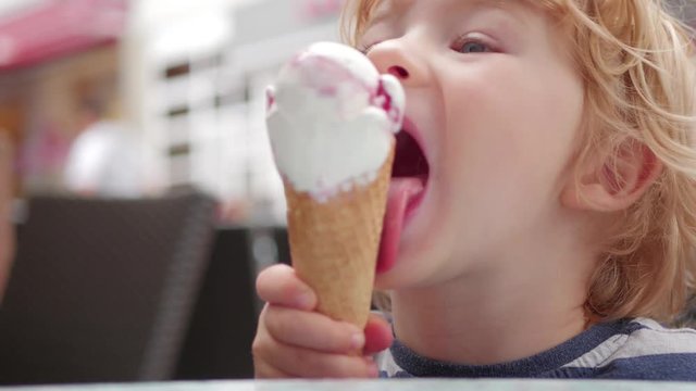 Young boy eating a tasty ice cream in cafe outdoor
Young boy with curly blonde hair eating a tasty cherry vanilla ice cream in cafe outdoor.